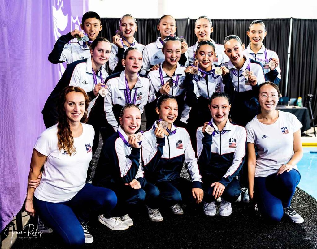 The USA Artistic Swimming Youth Team celebrate their win as 2022 FINA World Youth Artistic Swimming Champions with Head Coach Ludivine “Ludi” Perrin-Stsepaniuk  (far left- bottom) and Assistant Coach Xinya “Olivia” Zhang (far right- bottom)) 
Photo Credit: James Rokop-Rokop Photography 